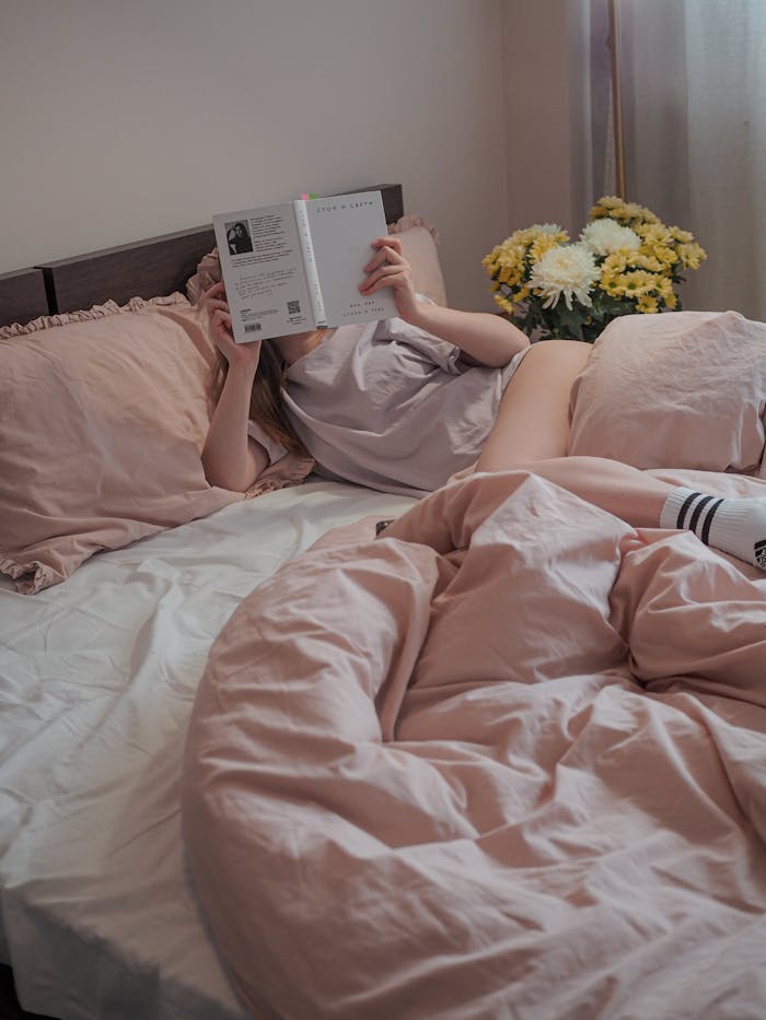 Woman enjoying a quiet morning reading in a cozy bedroom featuring soft pink bedding.