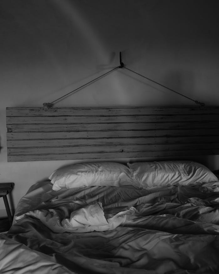 A minimalist black and white shot of an unmade bed with a rustic wooden headboard.