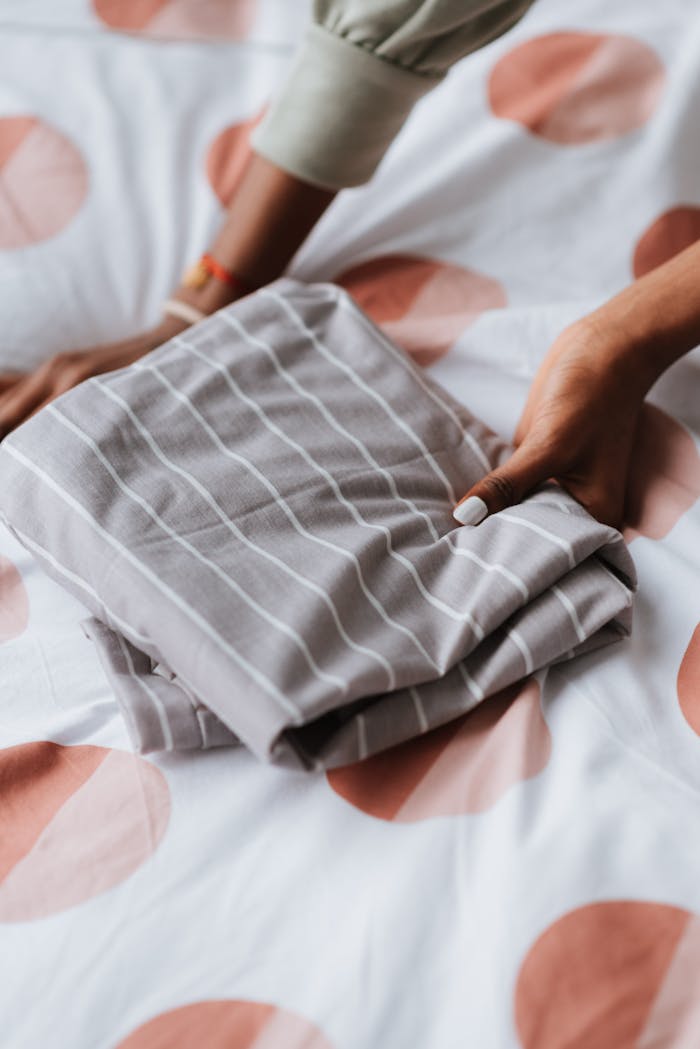 Crop unrecognizable ethnic female with folded wear with striped ornament on bed duvet at home